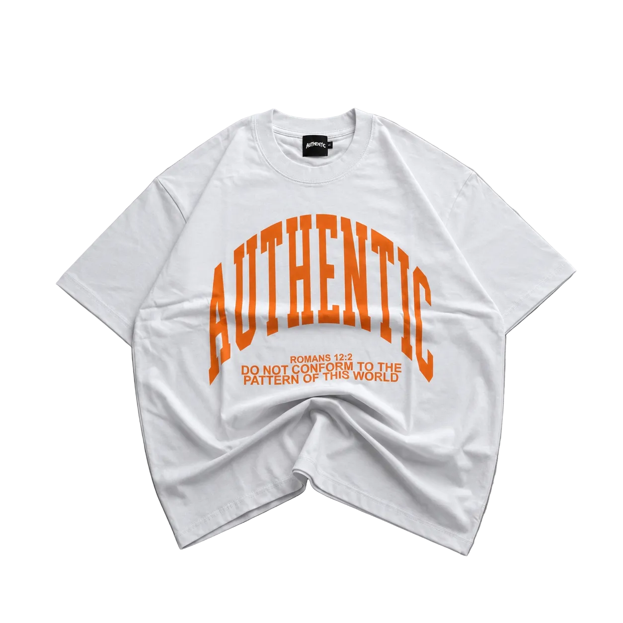 A white oversized short-sleeve t-shirt with a bold orange graphic reading 'AUTHENTIC' and smaller text below, laid flat on a gray concrete surface.